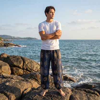Male model enjoying the breeze on beach rocks in black stonewashed organic cotton tribal harem pants.