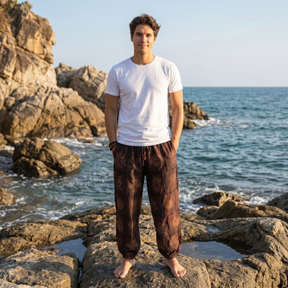 Male model standing on seaside rocks at a tropical beach wearing brown stonewashed organic cotton harem pants.