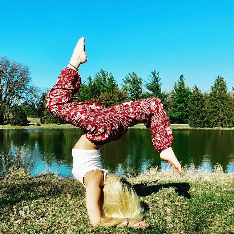 Person doing a handstand with one leg raised in a park by a lake in a Thai Elephant Harem Yoga Pants