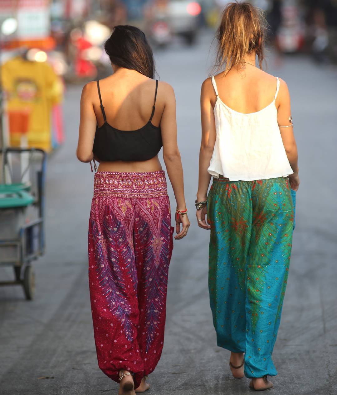 Two women in blue Thai harem yoga pants with peacock print and  white top walking on a street