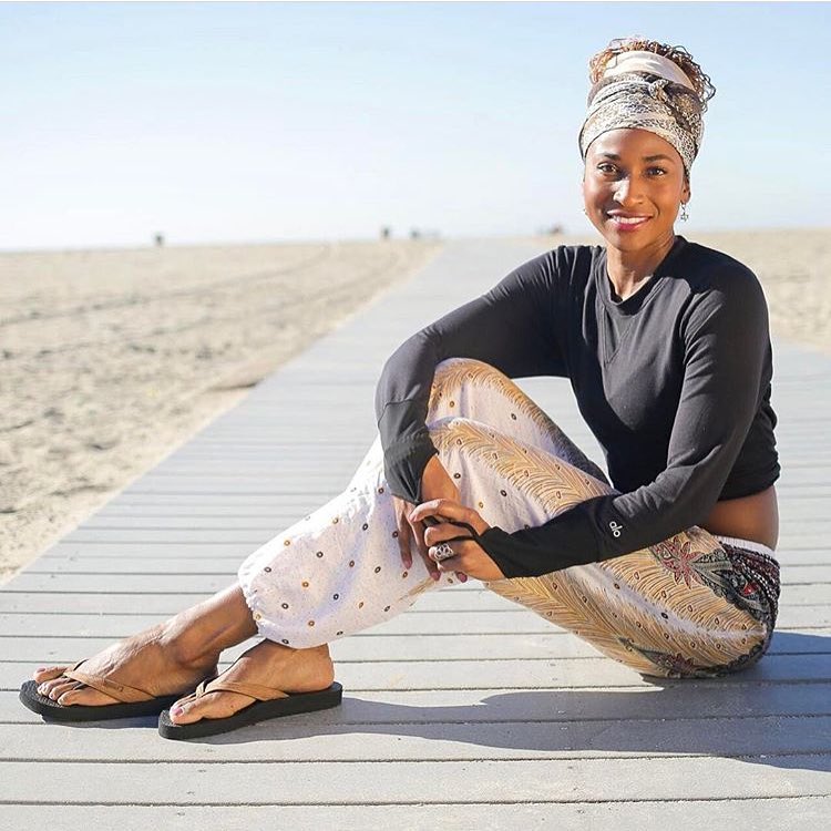 Woman sitting on a wooden boardwalk at the beach wearing a white Thai harem yoga pants with peacock print and black top