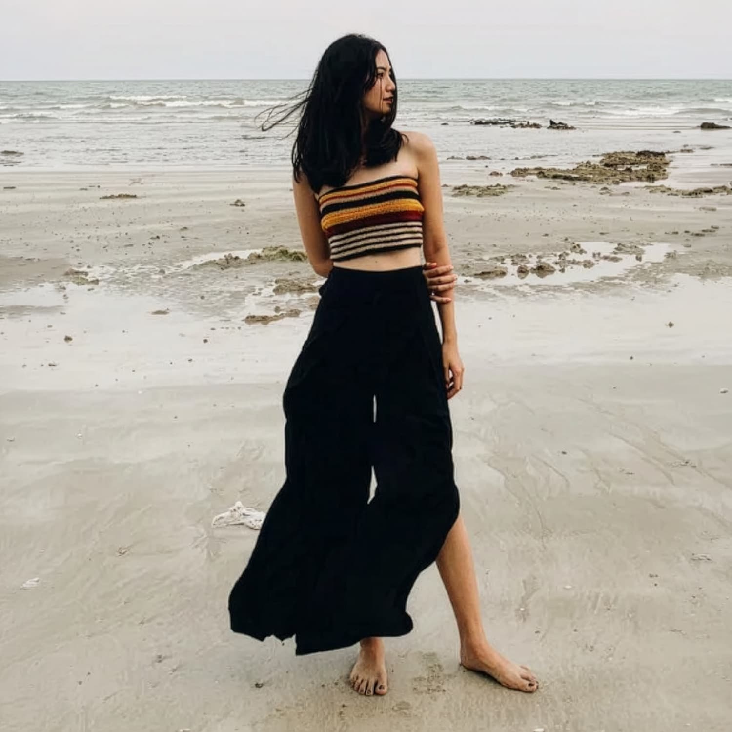 Woman in black thai wrap pants skirt and brown top standing on a thai beach