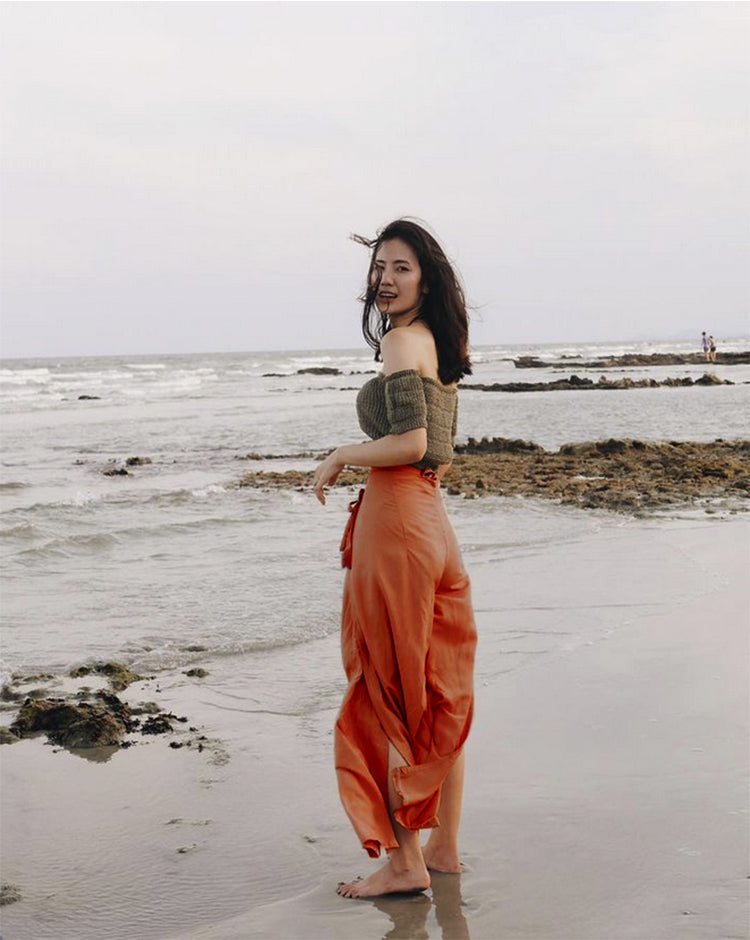 Woman in orange Thai wrap pants skirt and brown top standing on a Thai beach