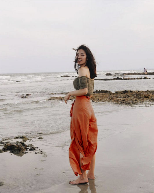 Woman in orange Thai wrap pants skirt and brown top standing on a Thai beach