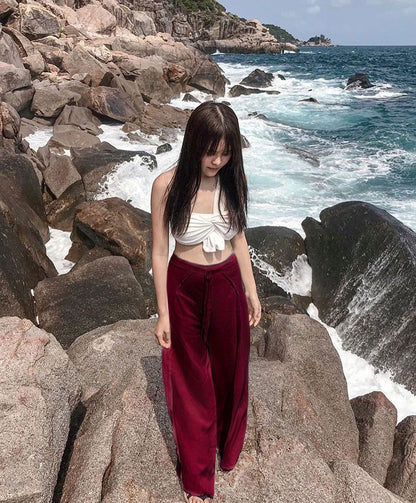 Woman wearing a maroon Thai Wrap Pants Skirt standing on rocky coastal area with ocean waves in the background