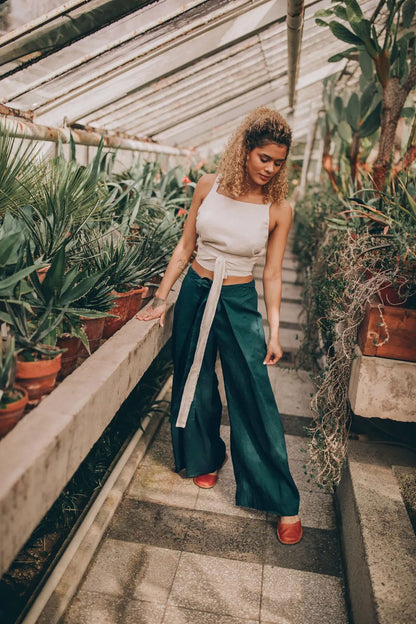 Woman in a white top and a turquoise Thai Wrap Pants Skirt walking through a greenhouse.