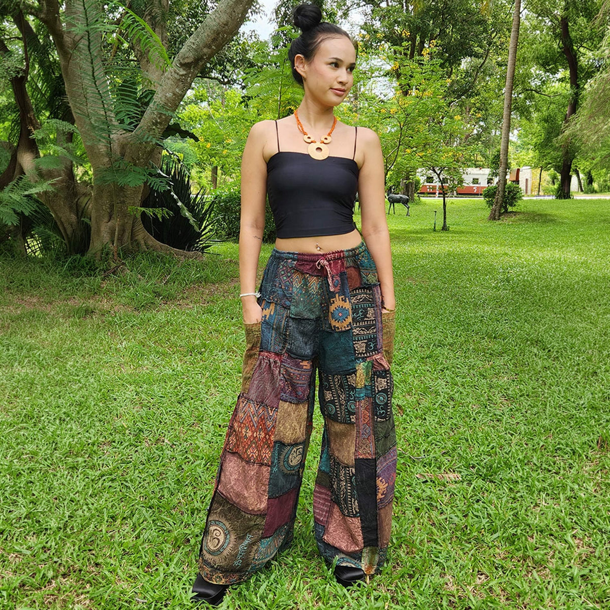 Female model wearing black patchwork wide-leg hippie palazzo boho pants in a park, front view.