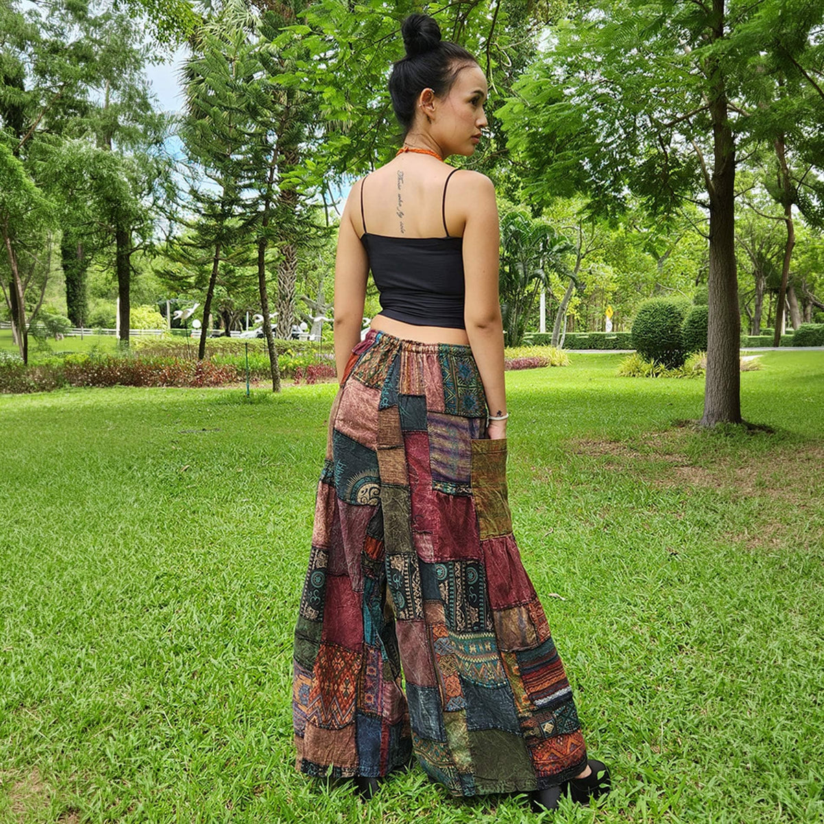 Back view of black patchwork wide-leg boho palazzo pants worn by a model in a park.