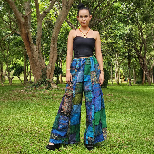 Woman wearing blue patchwork wide-leg boho palazzo pants standing in a park, front view.