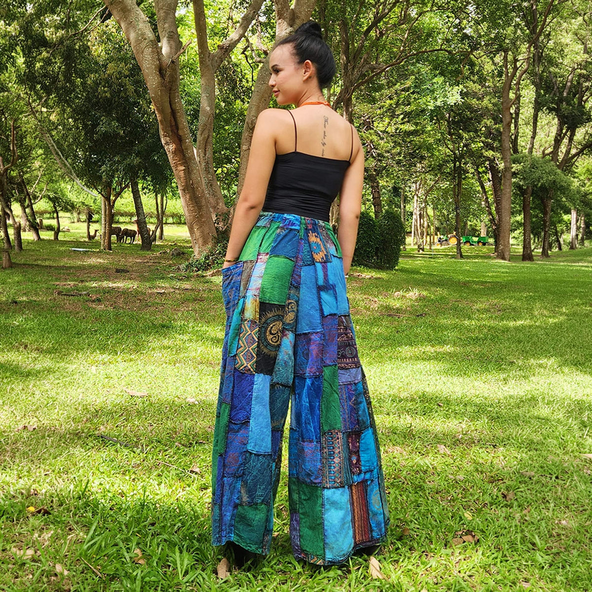 Back view of a woman in blue wide-leg boho patchwork palazzo pants in a natural park setting.