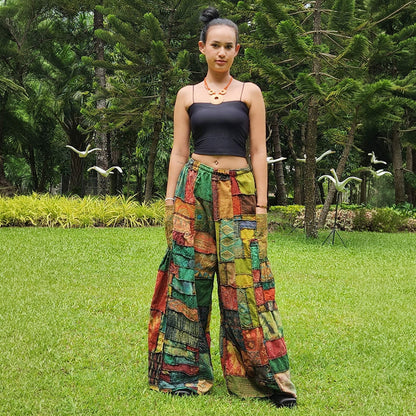 Female model wearing brown patchwork wide-leg boho palazzo pants standing in a sunny park, front view.