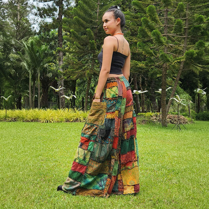 Female model wearing brown boho patchwork wide-leg palazzo pants in a park, back view showing the relaxed fit.