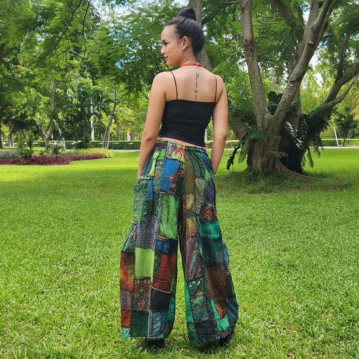 Back view of a woman wearing green patchwork wide-leg palazzo boho pants outdoors in a park.