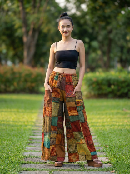 Woman wearing colorful patchwork hippie palazzo pants and a black top standing on a path with greenery in the background