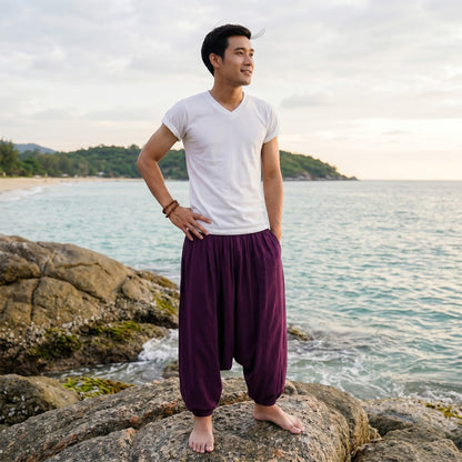 Male model standing on rocks by the ocean wearing deep purple Men's drop crotch harem pants.