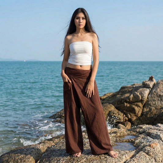 Female model standing confidently on rocks by the ocean, wearing versatile Earthy Brown women's Thai fisherman pants.