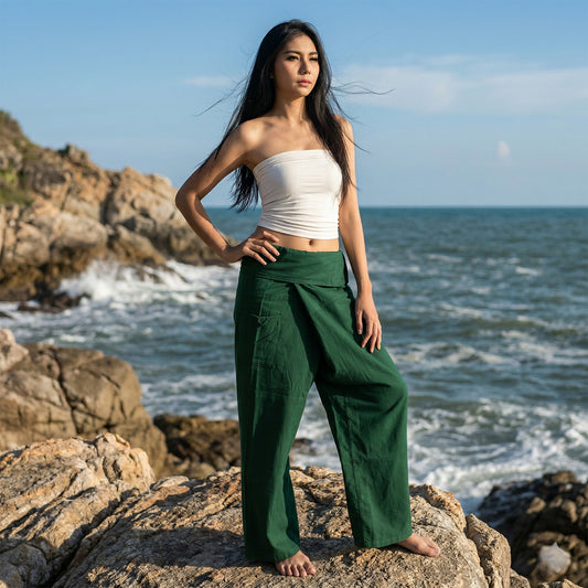 Female model standing confidently on rocks by the ocean, wearing versatile Forest Green Oasis women's Thai fisherman pants.