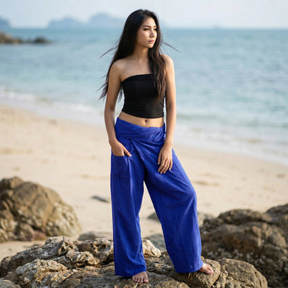 Female model standing confidently on rocks by the ocean, wearing versatile Oceanic Navy women's Thai fisherman pants.