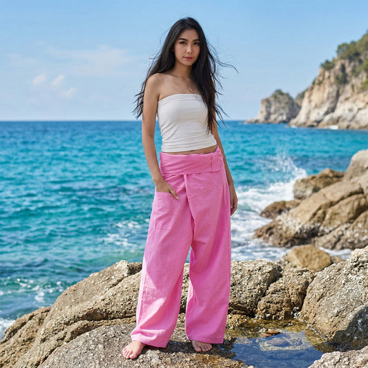 Female model standing confidently on rocks by the ocean, wearing versatile Pink Paradise women's Thai fisherman pants.