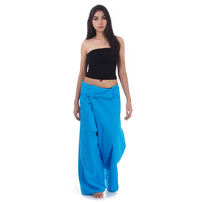 Female model standing confidently on rocks by the ocean, wearing versatile Sky Blue Horizon women's Thai fisherman pants.
