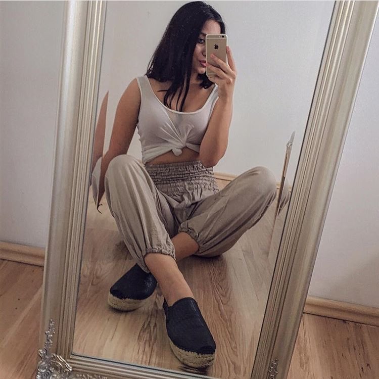 Person taking a mirror selfie wearing a white top and beige my thai harem pants, sitting on the floor.