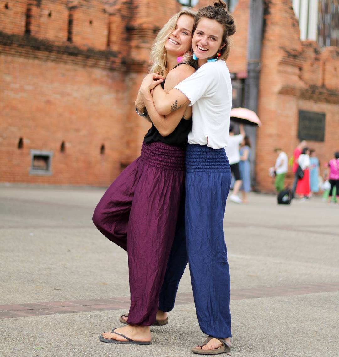 Two women hugging in front of a brick building my thai harem pants