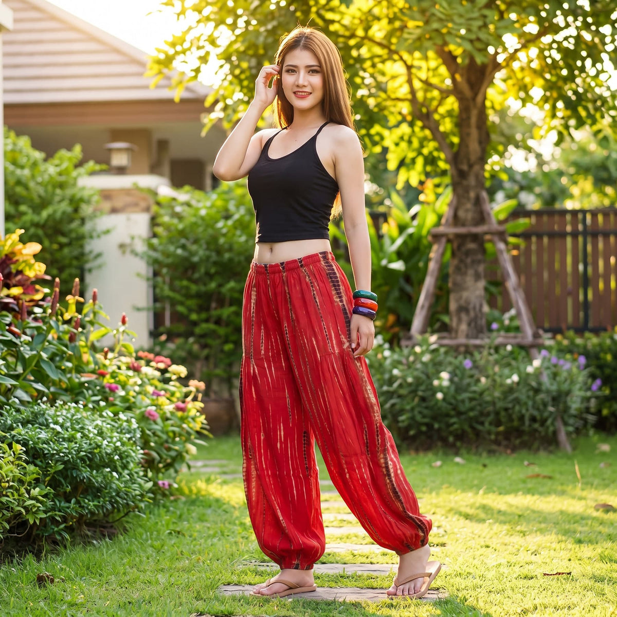 Female model posing outdoors in a green garden setting wearing the eye-catching Women's Tie Dye Harem Pants Vibrant Red.
