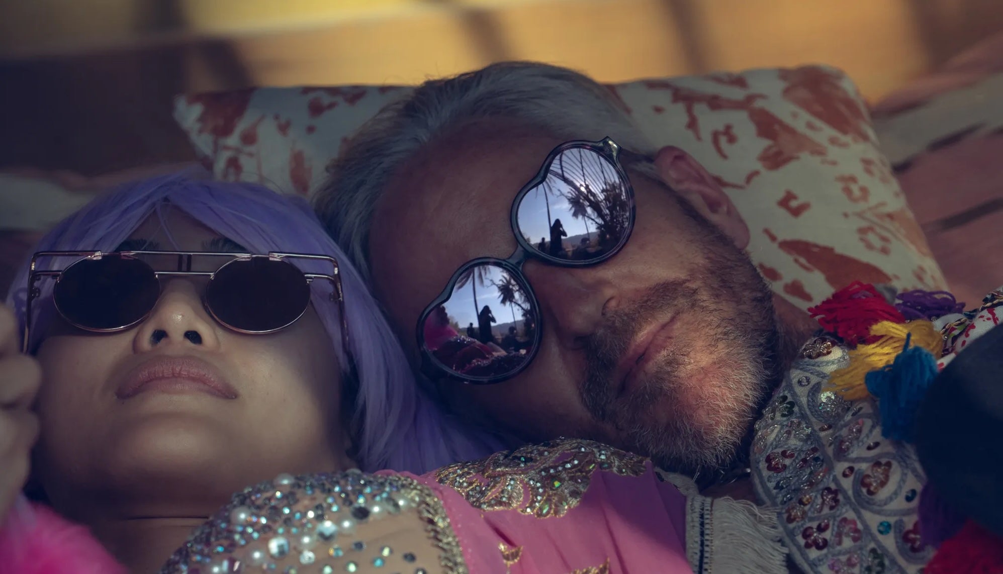 Two people lying down with sunglasses on, one with purple hair and the other with a colorful outfit on Tomorrowland Thailand Festival