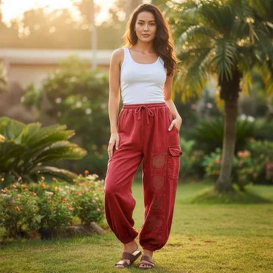 Female model wearing red boho tribal mandala harem pants in a sunny park, front view.