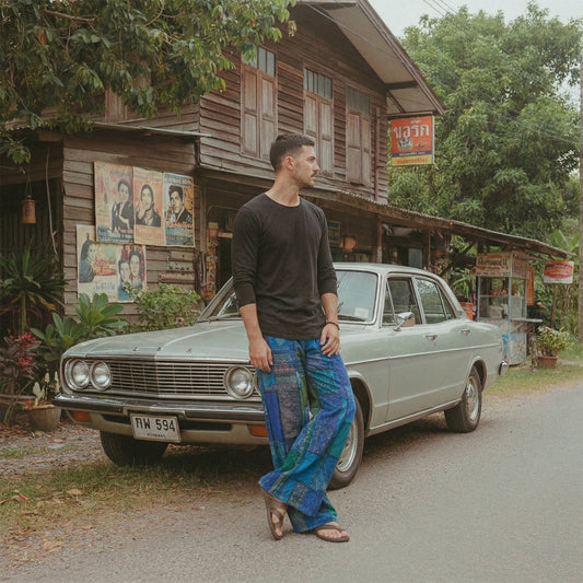 Male model posing in blue boho patchwork pants with a vintage car in an authentic Thai village setting.