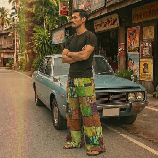 Man posing in olive boho patchwork pants next to a classic car at a traditional Thai grocery store.