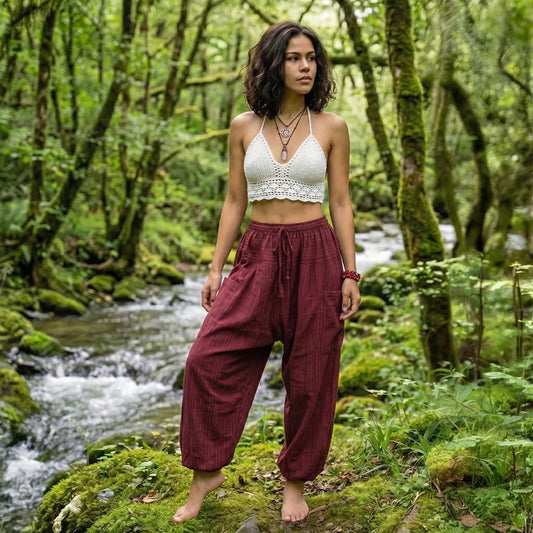 Female model in Sunset Maroon pinstripe pants by a forest stream, reflecting a bohemian lifestyle.