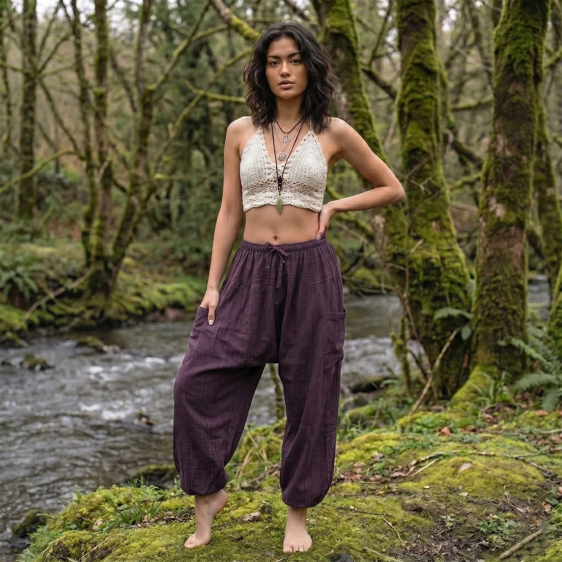 Female model wearing Purple Orchid pinstripe pants in a serene forest setting by a flowing stream.