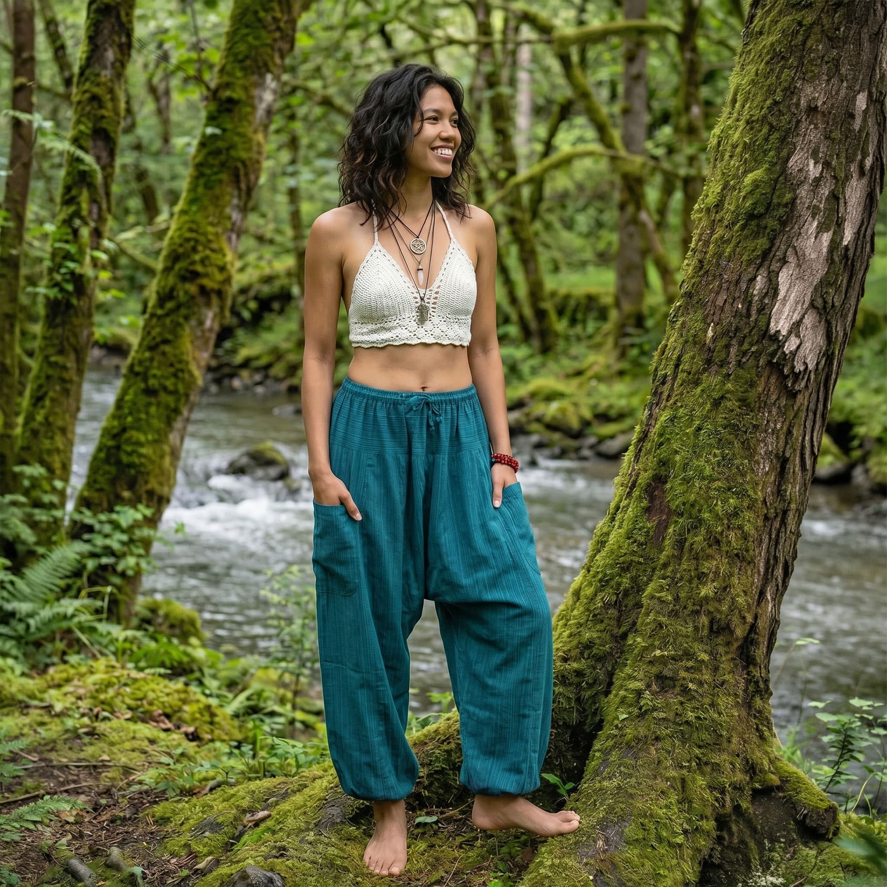Female model wearing Turquoise Bay pinstripe harem pants in a forest setting by a flowing stream, showcasing the airy and flowy nature of the cotton.