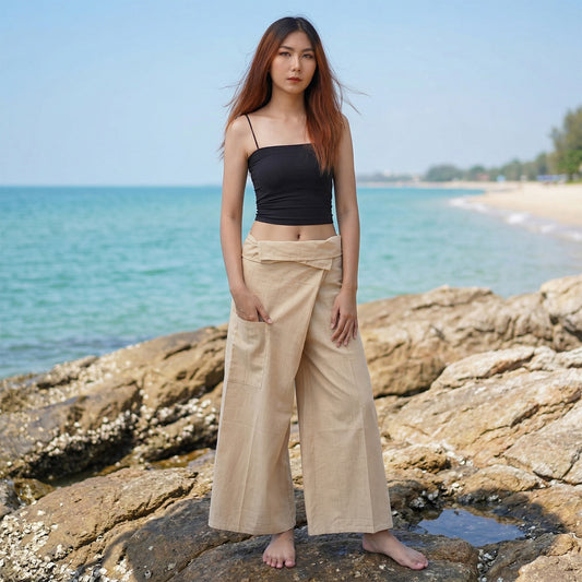 Female model standing confidently on rocks by the ocean, wearing versatile Sandy Beige women's pinstripe Thai fisherman pants.
