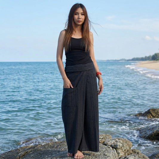 Female model standing confidently on rocks by the ocean, wearing versatile Black Sand women's pinstripe Thai fisherman pants.