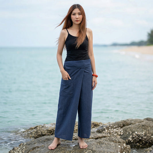 Female model standing confidently on rocks by the ocean, wearing versatile Blue Lagoon women's pinstripe Thai fisherman pants.