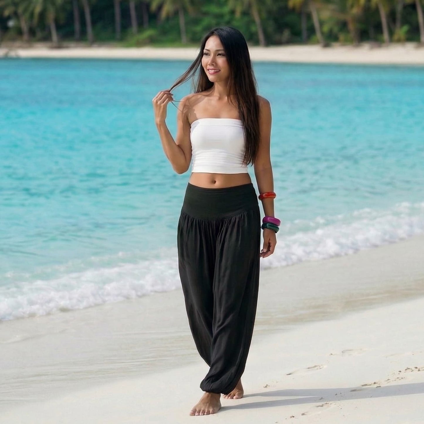 Female model in midnight black Thai harem pants walking on a Thai beach, showcasing the unique handcrafted sophistication and movement.