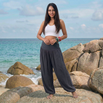 Female model in elephant gray Thai harem pants walking on a Thai beach, highlighting the classic handmade color and nature-inspired flow.