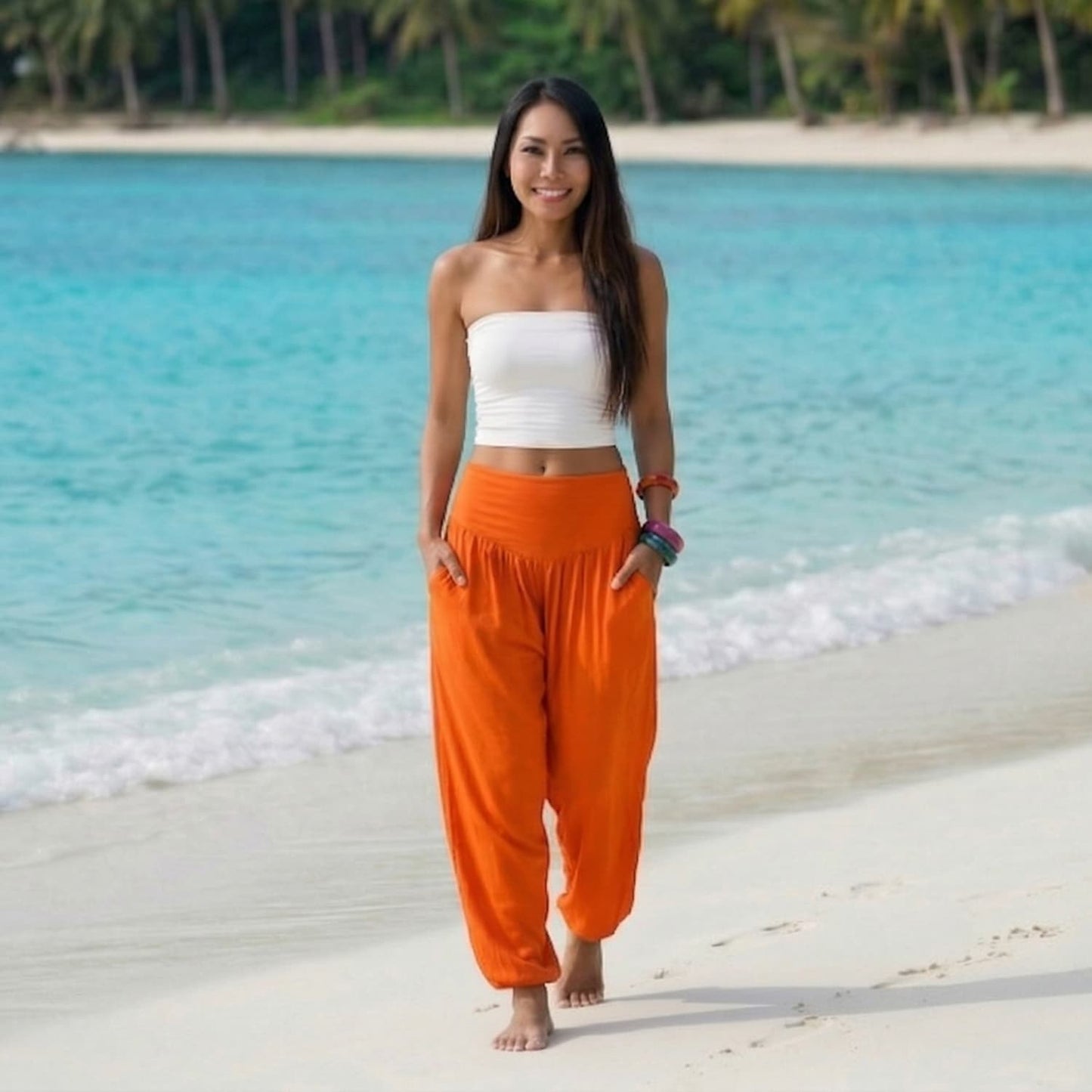 Female model in mango tango Thai harem pants walking on a Thai beach, highlighting the vibrant tropical color and textile flow.