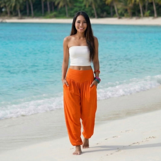 Female model in mango tango Thai harem pants walking on a Thai beach, highlighting the vibrant tropical color and textile flow.